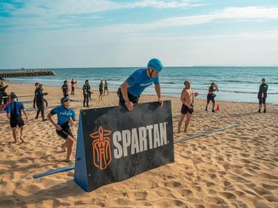 Gara Spartan sulla spiaggia con ostacoli e partecipanti.