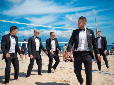 Uomini in smoking giocano a beach volley sulla spiaggia.