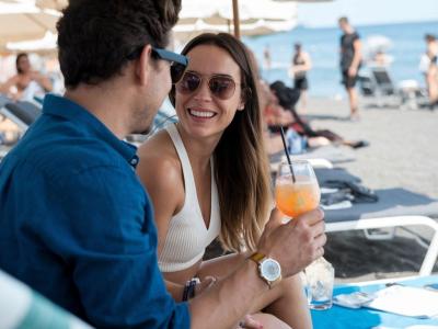 Coppia sorridente in spiaggia, bevendo cocktail sotto l'ombrellone.