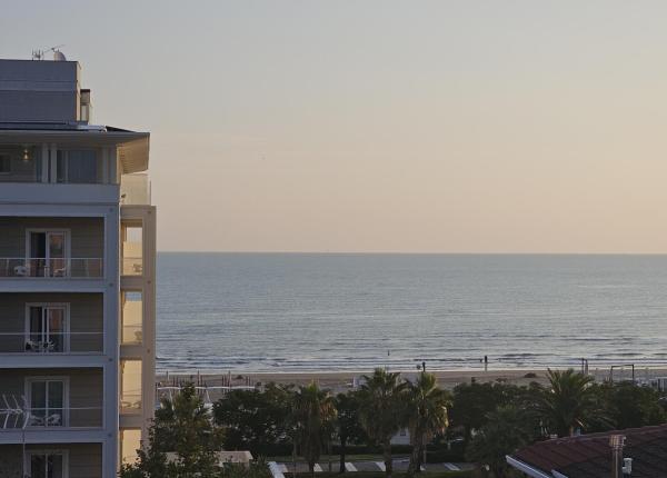 Vista mare al tramonto con palme e edifici.