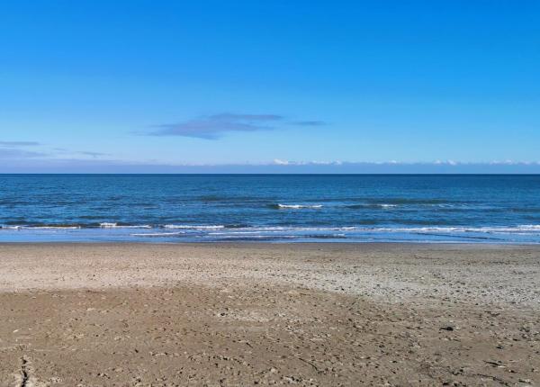 Spiaggia sabbiosa con mare calmo e cielo azzurro.