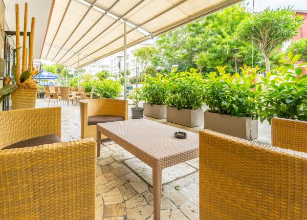 Terrazza con sedie di vimini e piante, sotto un tendone.