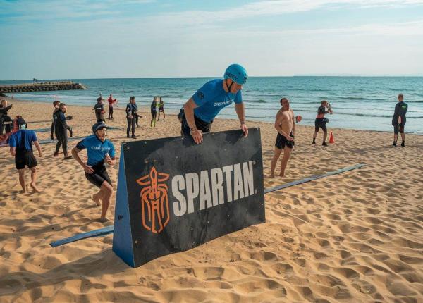 Gara Spartan sulla spiaggia con ostacoli e partecipanti.