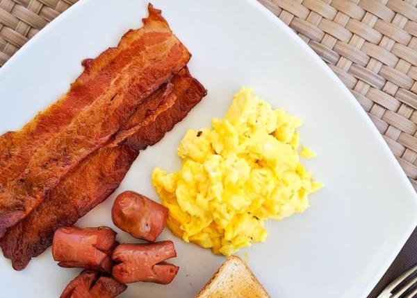 Colazione con uova, pancetta, toast e yogurt con frutta.