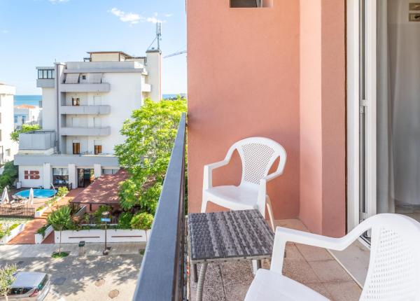 Balcone con sedie bianche, tavolino e vista su edifici e piscina.