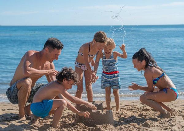 Famiglia costruisce castello di sabbia sulla spiaggia, giornata di sole e divertimento.