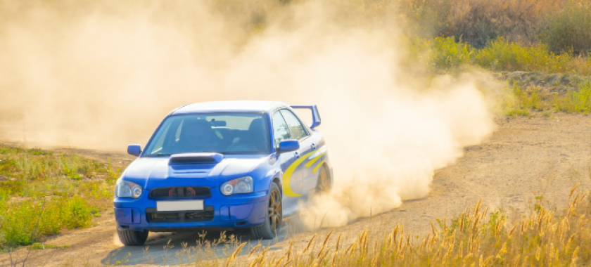 Auto blu da rally su strada sterrata, sollevando polvere.