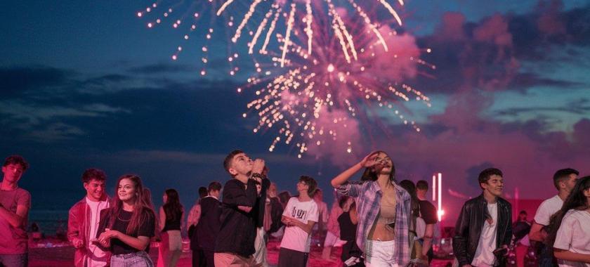 Festa in spiaggia con fuochi d'artificio e giovani che ballano.