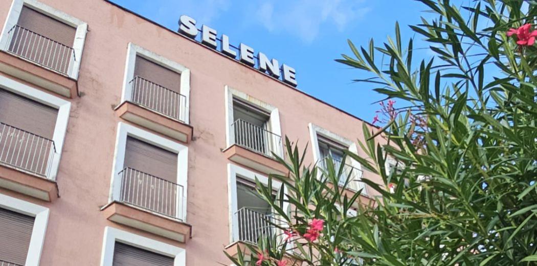 Edificio rosa con insegna 'SELENE' e piante fiorite in primo piano.
