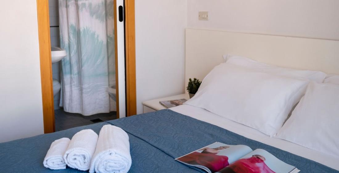 Camera da letto con bagno, letto matrimoniale, asciugamani e rivista su coperta blu.