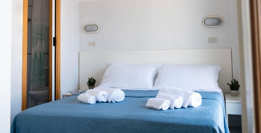 Camera da letto con letto matrimoniale, lenzuola bianche, asciugamani e bagno privato.