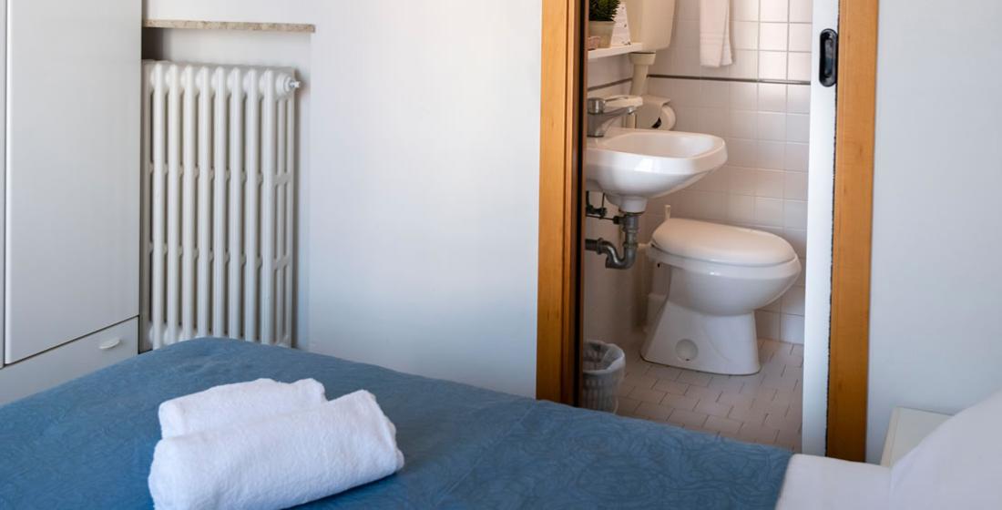 Camera da letto con bagno privato, asciugamani sul letto, radiatore e porta scorrevole.
