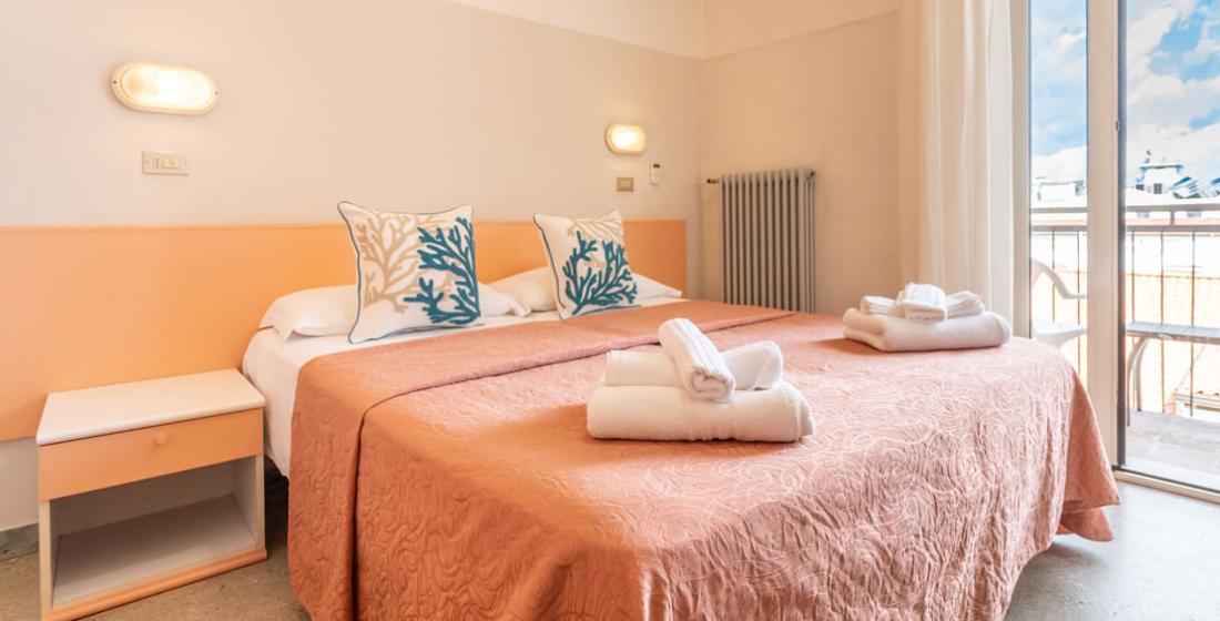 Camera da letto luminosa con letto matrimoniale, cuscini decorati e asciugamani piegati.
