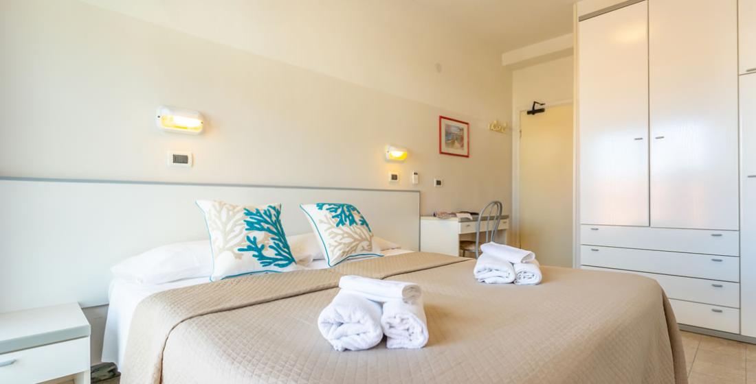 Camera da letto luminosa con letto matrimoniale, cuscini decorativi e asciugamani piegati.
