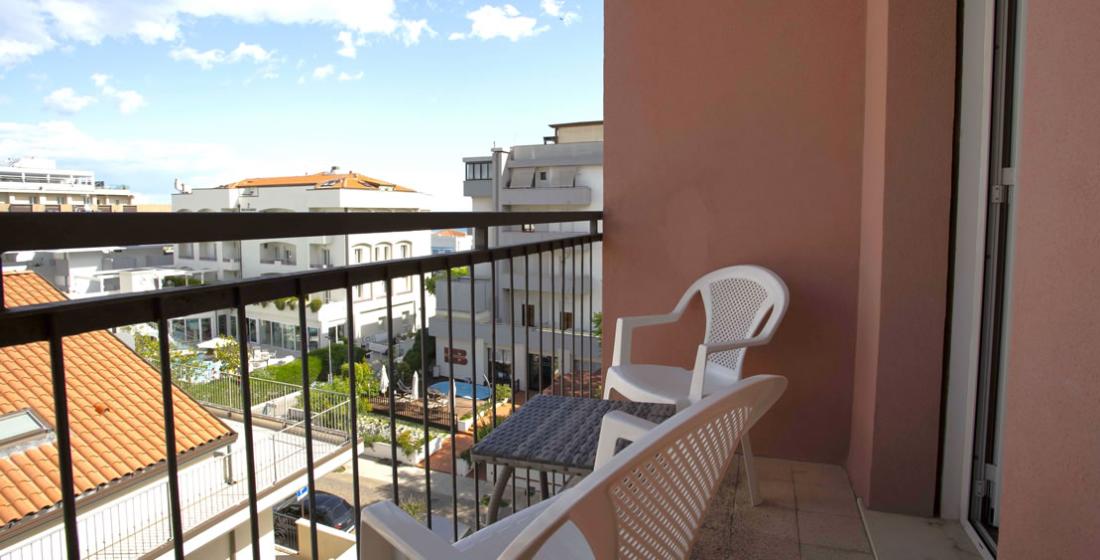 Balcone con sedie bianche, tavolo e vista su edifici residenziali.