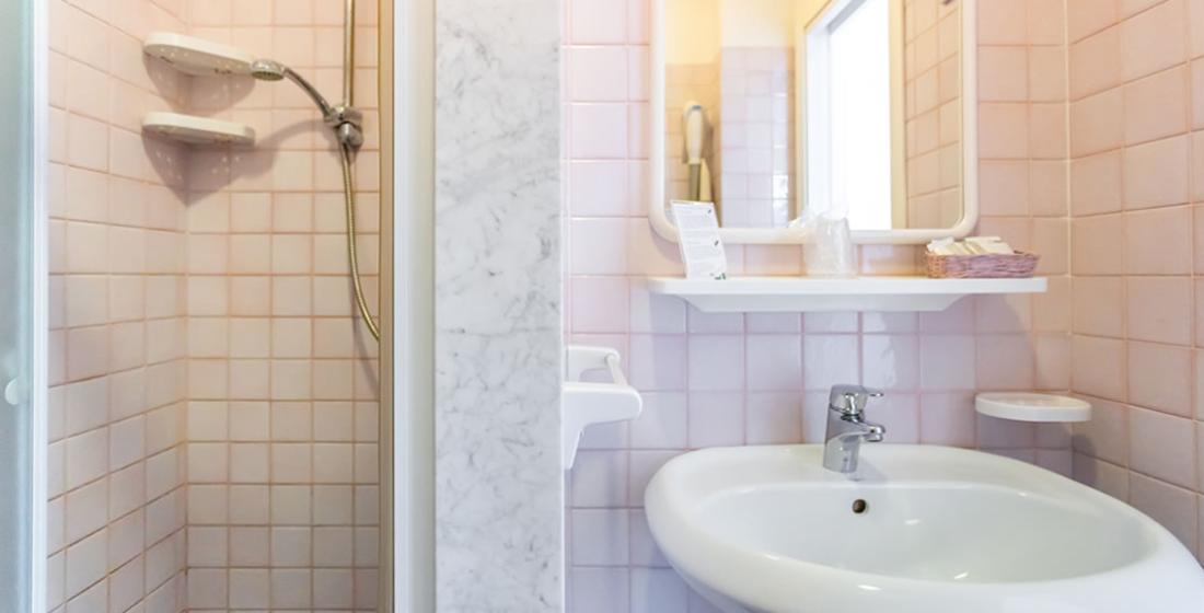 Bagno con doccia, lavandino, specchio e piastrelle rosa chiaro.