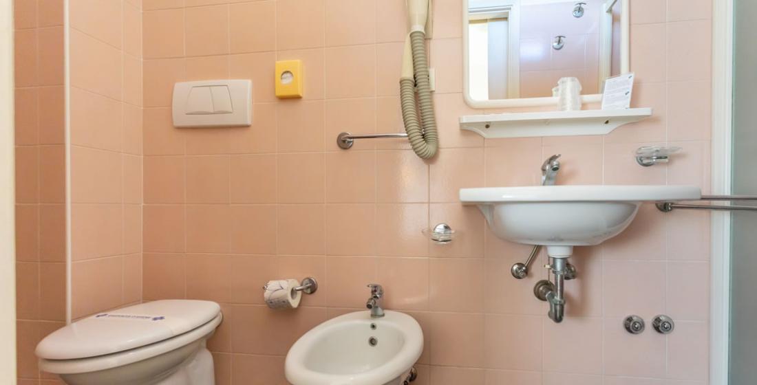 Bagno con bidet, lavandino, specchio, asciugacapelli e piastrelle rosa chiaro.