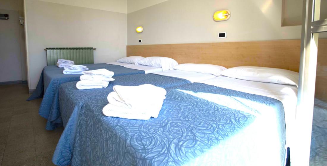 Camera con letti singoli, coperte blu e asciugamani bianchi piegati.