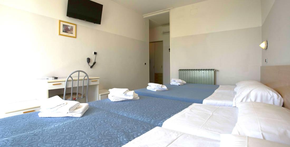Camera d'albergo con letti singoli, TV a parete e scrivania.
