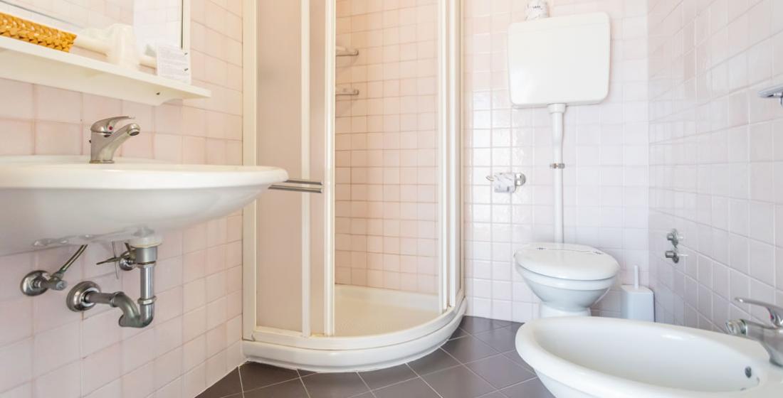Bagno con doccia, lavandino, bidet e WC su piastrelle bianche e grigie.