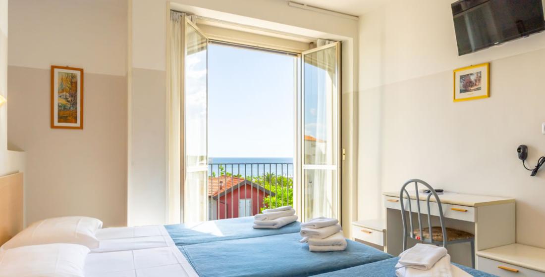 Camera luminosa con vista mare, letto matrimoniale e balcone aperto.