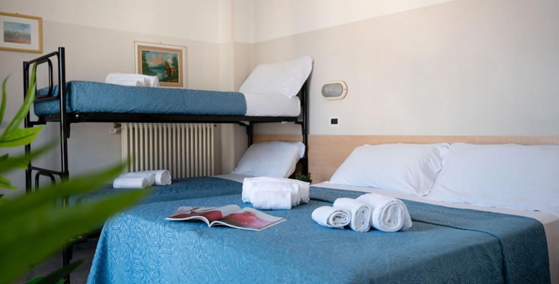 Camera con letto matrimoniale e a castello, lenzuola blu e asciugamani bianchi.