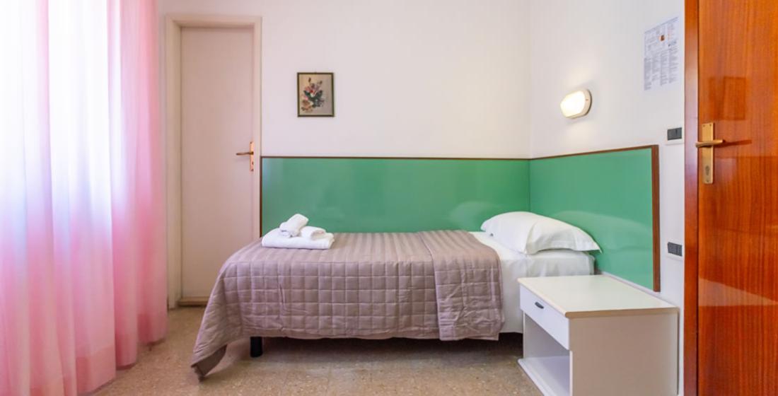 Camera singola con letto, comodino e pareti verde pastello.