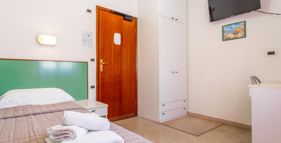 Camera semplice con letto, armadio, TV e asciugamani piegati.
