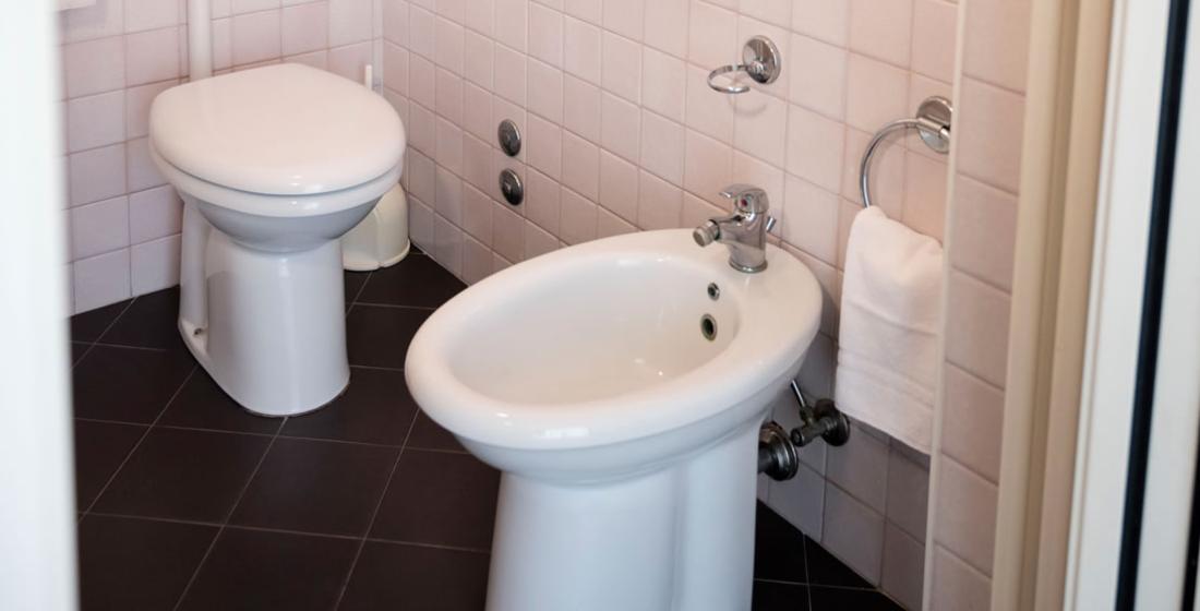 Bagno con WC e bidet, piastrelle rosa e pavimento scuro.