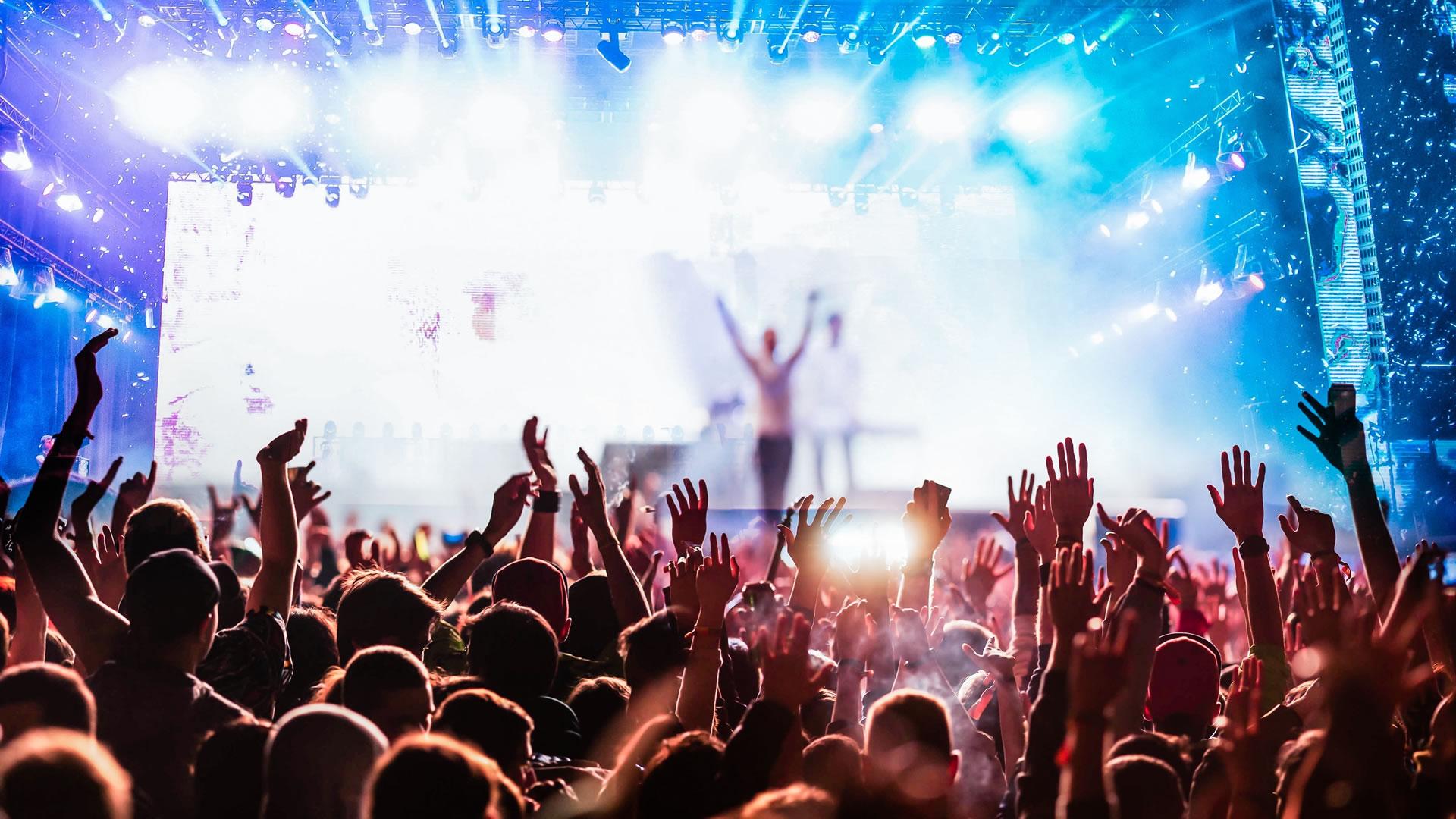 Concerto dal vivo con folla entusiasta e luci colorate sul palco.