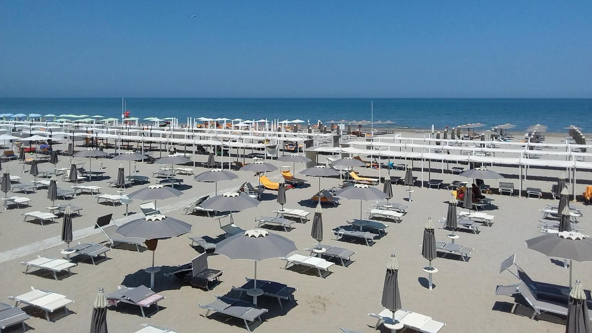 Spiaggia con ombrelloni e lettini, persone che si rilassano al sole vicino al mare.