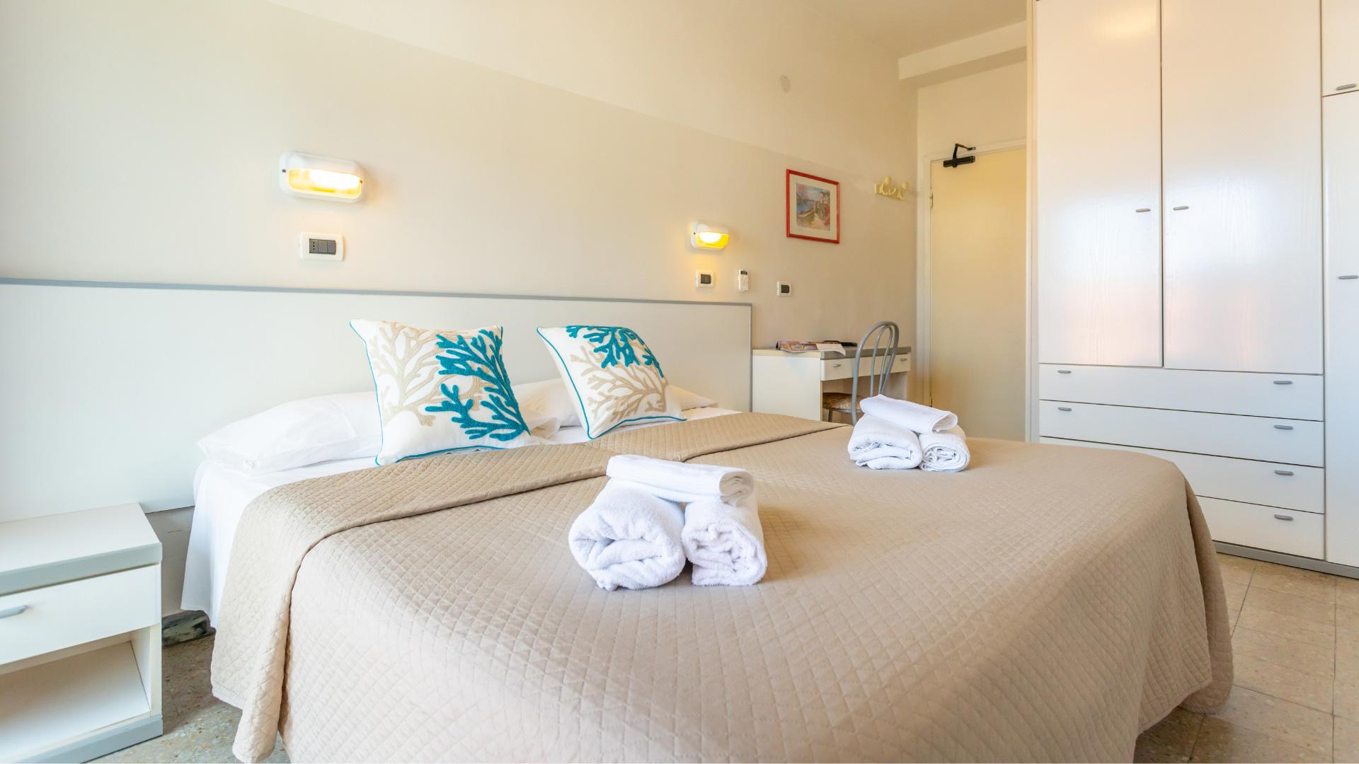 Camera luminosa con letto matrimoniale, cuscini decorativi e armadio bianco.