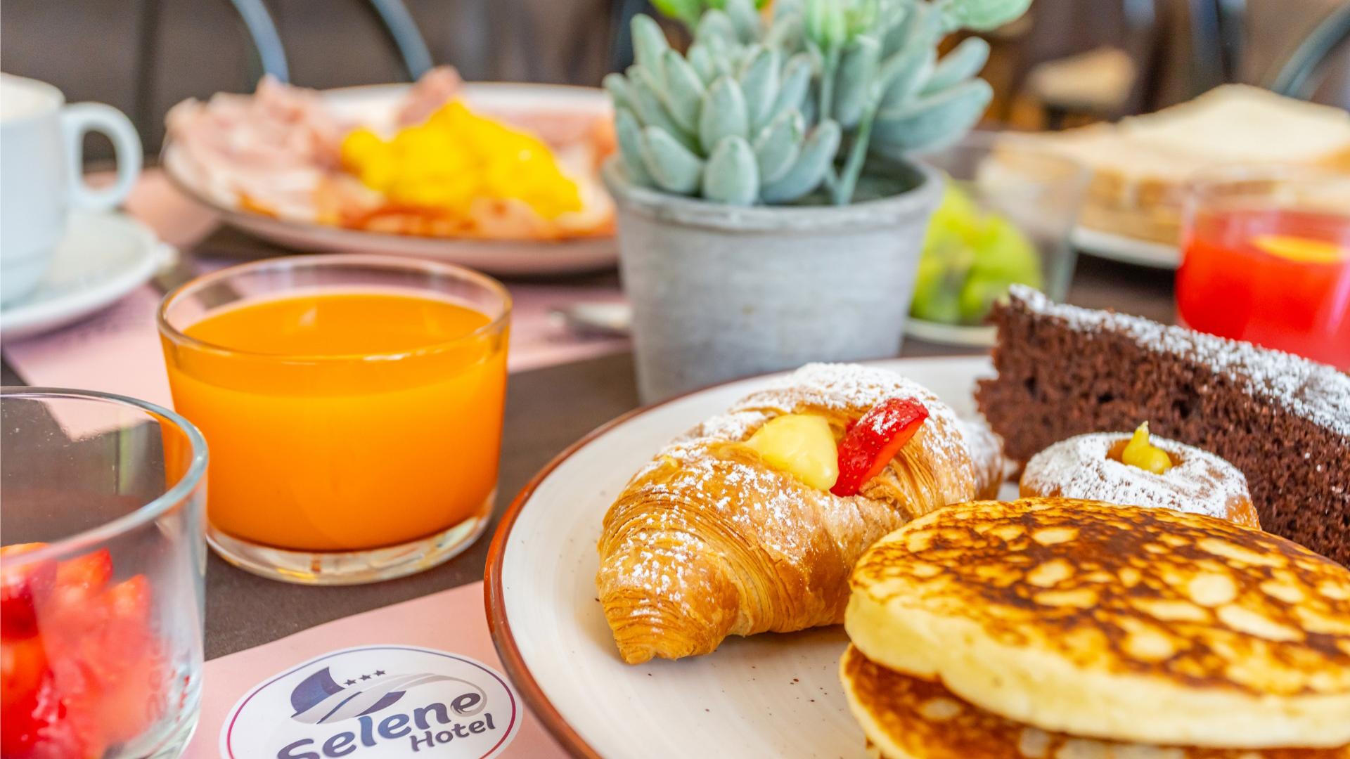 Colazione con croissant, pancake, torta al cioccolato e succo d'arancia in hotel.