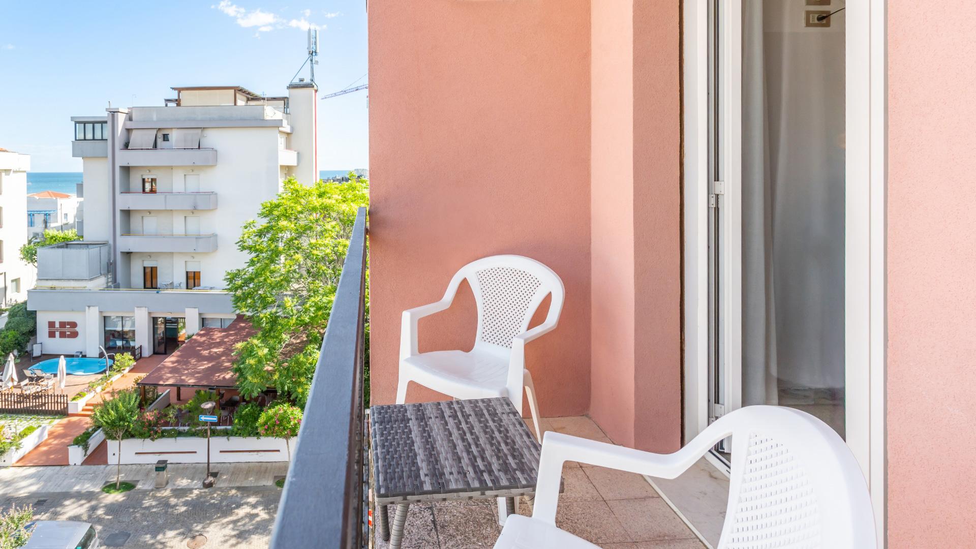 Balcone con sedie bianche e tavolino, vista su edificio e mare.