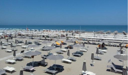 Spiaggia con ombrelloni e lettini, mare calmo e cielo sereno.