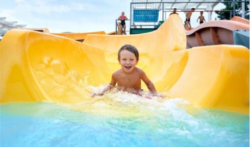 Bambino felice scivola su uno scivolo d'acqua giallo in un parco acquatico.