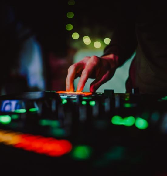 DJ che mixa musica con una console, luci colorate sullo sfondo.