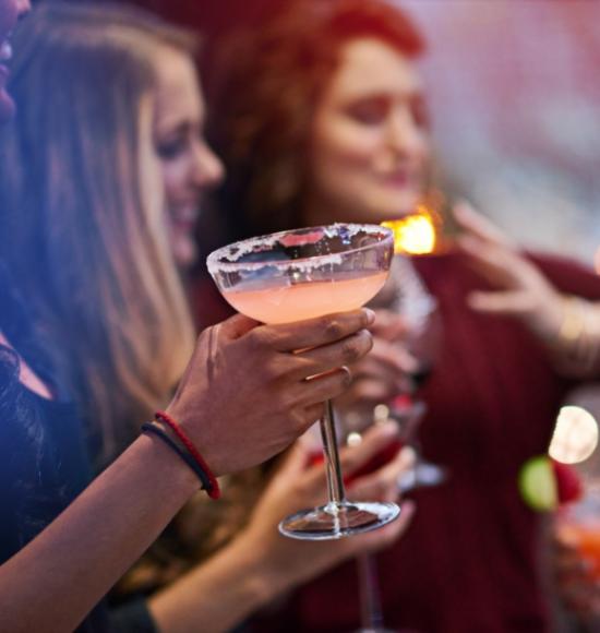 Persone festeggiano con cocktail in mano, atmosfera vivace e allegra.
