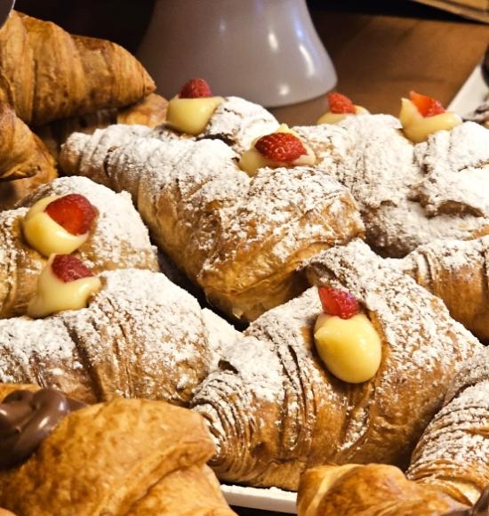 Cornetti ripieni di crema pasticcera e fragole, spolverati con zucchero a velo.