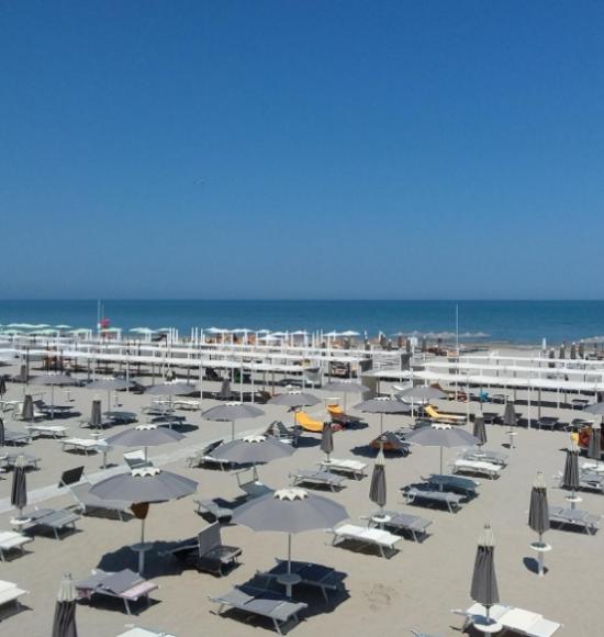 Spiaggia con ombrelloni e lettini sotto un cielo limpido e mare calmo.