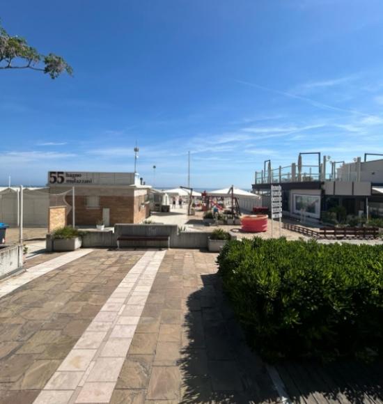 Spiaggia con stabilimento balneare, cielo sereno e mare in lontananza.
