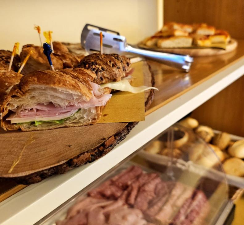 Panino con prosciutto e formaggio su tagliere di legno, con pane ai semi.
