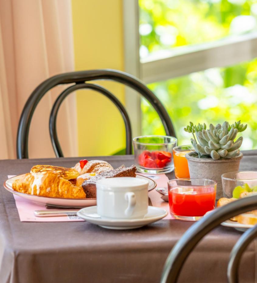 Colazione con croissant, succo, tazza di caffè e pianta grassa su tavolo.