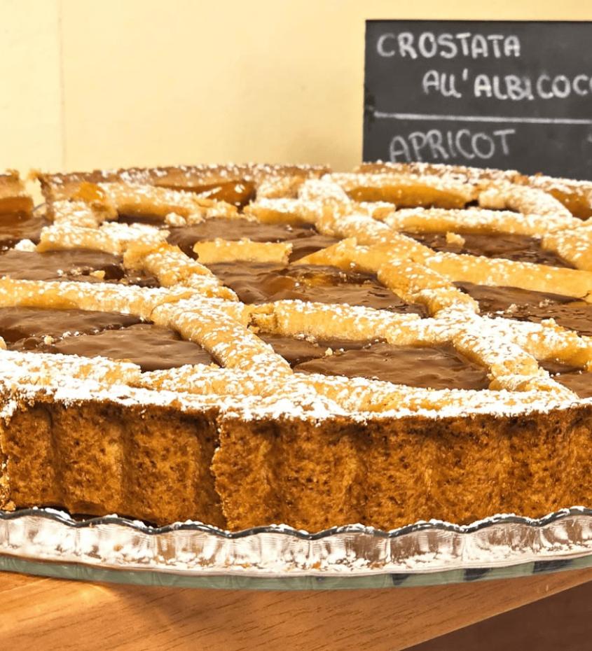 Crostata all'albicocca con zucchero a velo su piatto di vetro, etichetta descrittiva sullo sfondo.