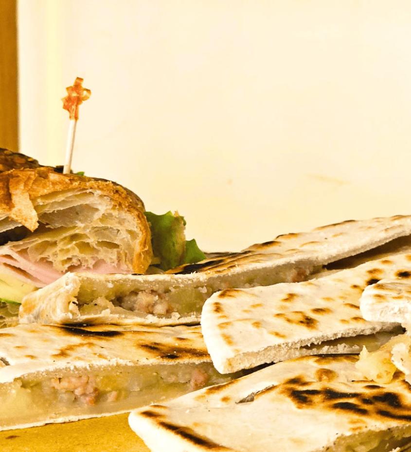 Piadine e croissant farciti con prosciutto e formaggio, serviti su un piatto.