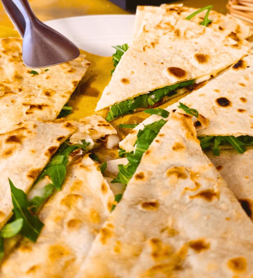 Piadina farcita con rucola e formaggio, tagliata a spicchi su un piatto.