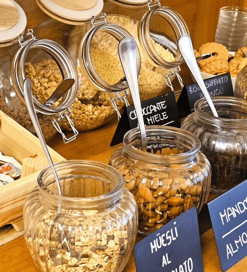 Dispensa con cereali, mandorle, uva sultanina e Nutella in vasetti di vetro.