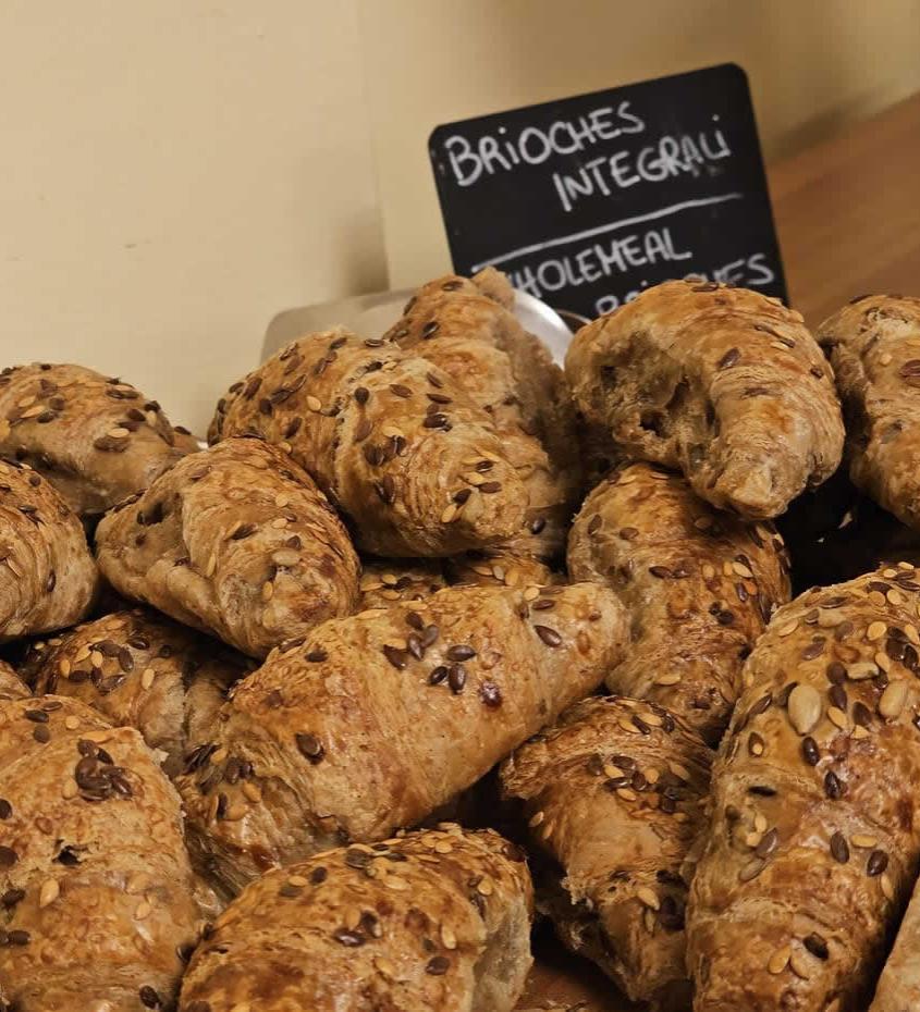 Brioches integrali con semi, esposte su un bancone di una panetteria.