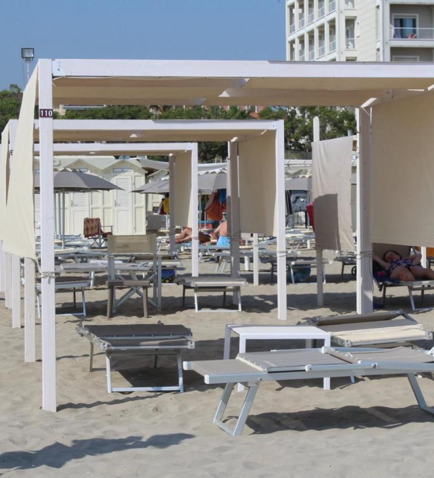 Spiaggia con lettini e cabine, persone rilassate sotto ombrelloni e tende.